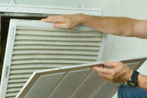 How Do Air Purifiers and Air Filters Work? Professional repair service man or diy home owner removing a dirty air filter on a house air conditioner so he can replace it with a new clean one.