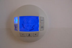 How to Set Your Programmable Thermostat. Photo of a digital thermostat mounted on a wall with a blue light.