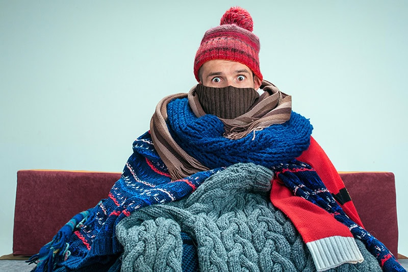 How to Keep Warm During Extreme Cold Weather. A woman bundled up in blankets and scarves.
